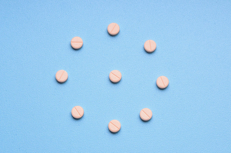 Pink tablet of medicine against light blue background, studio shot