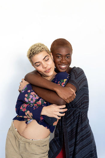 Portrait of smiling lesbian couple embracing against white background