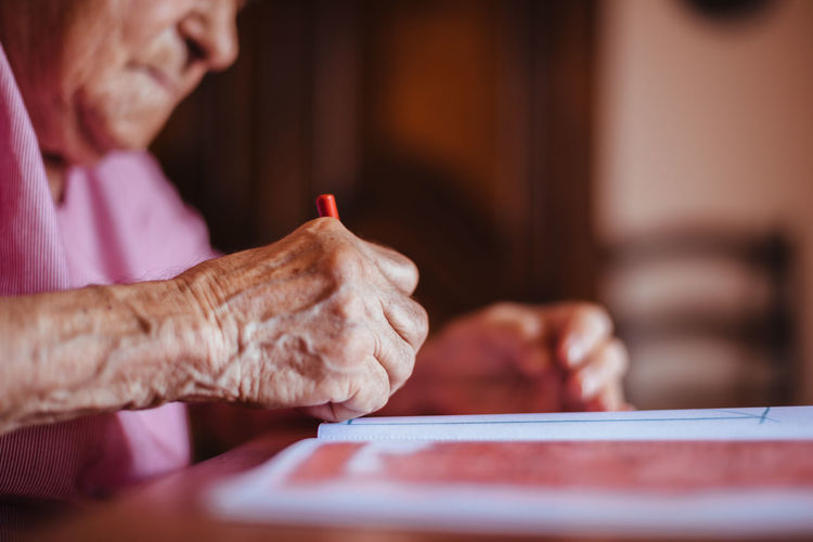 Side view of a senior woman with alzheimer's mental health issues painting on a notebook inside her home