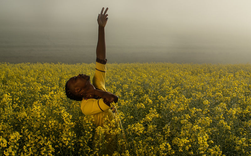 Man with arms raised standing on yellow flower field