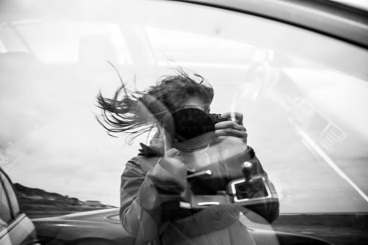 Reflection of woman photographing with camera on car window