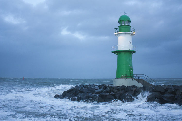 Lighthouse in sea against cloudy sky