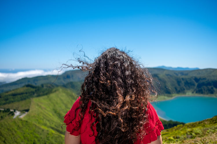 Rear view of woman standing on mountain against clear blue sky