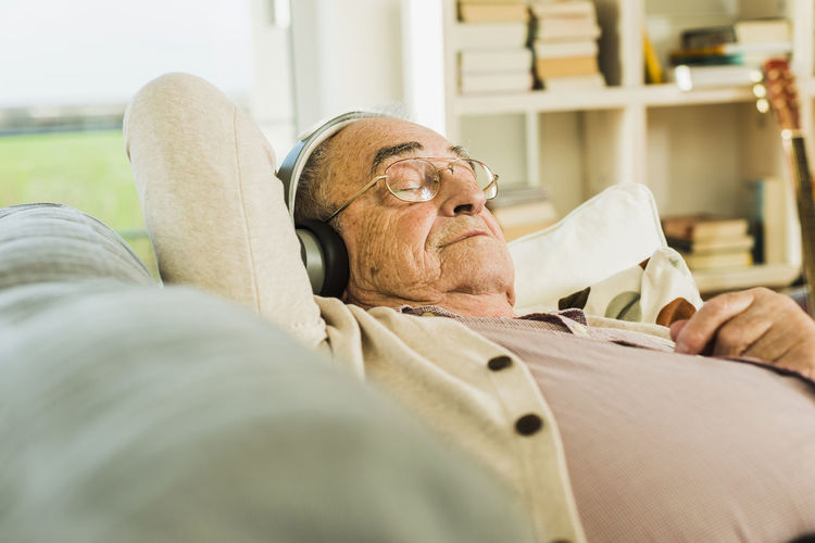 Senior man lying on the couch hearing music with headphones