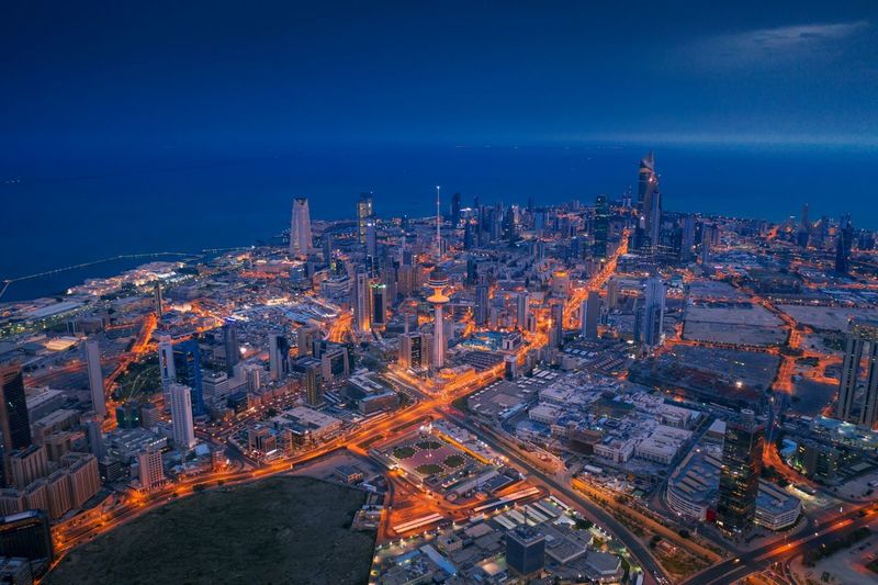 Aerial view of illuminated cityscape by seascape against blue sky at dusk