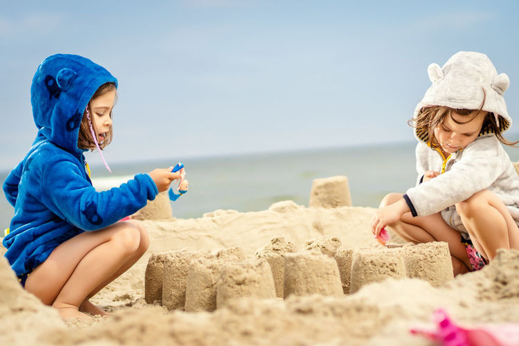 Siblings making sandcastle while crouching at beach