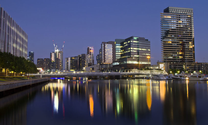 Illuminated buildings by river against sky in city