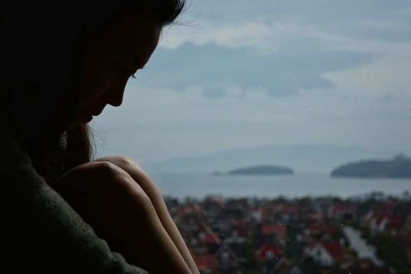 Close-up of woman hugging knees sitting by sea against sky