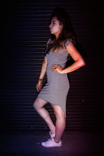 Beautiful young woman standing against wall at night