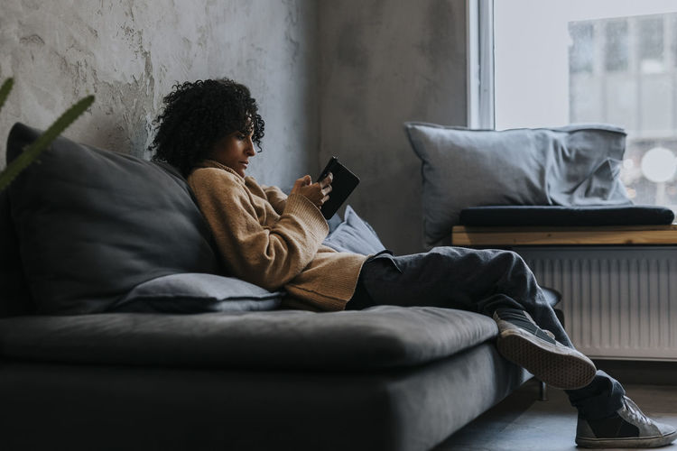 Young woman using laptop while lying on sofa at home