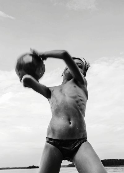 Low angle view of shirtless kid holding ball against sky
