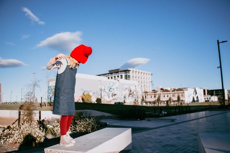 Full length of girl standing on bench against buildings in city