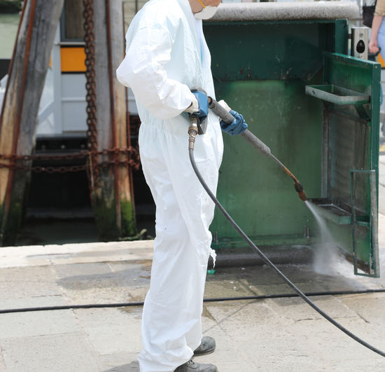 Worker with the jet of the pressure washer of the trash bin during the quarantine by corona virus