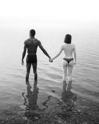 Rear view of shirtless man and woman standing on beach