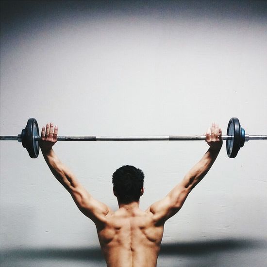 Rear view of muscular man lifted barbell against wall
