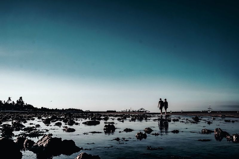 Silhouette couple walking at beach against blue sky during sunset