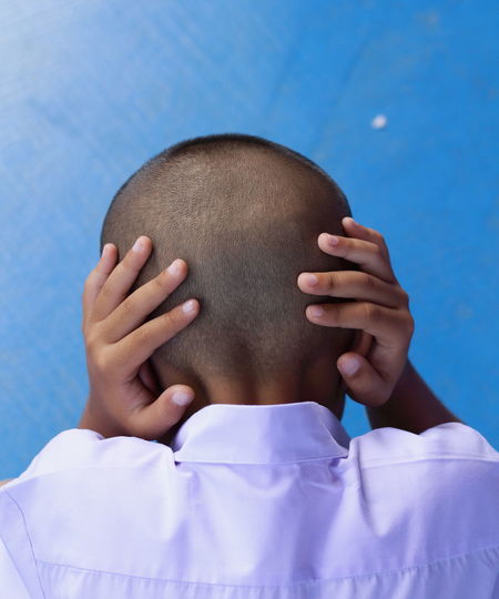Rear view of boy covering ears against blue wall