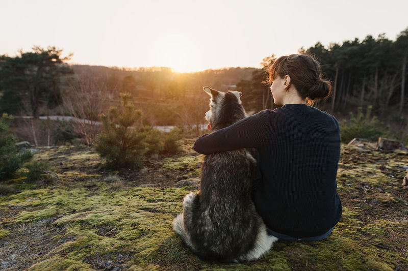 Rear view of woman with dog sitting against sky during sunset