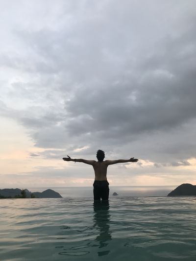 Man with arms outstretched standing in sea against cloudy sky