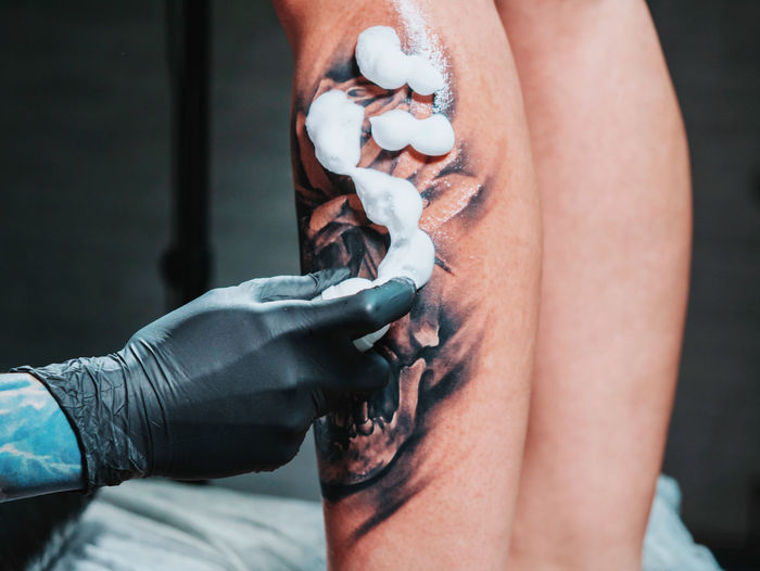 Cropped image of tattooist applying cream on customer leg