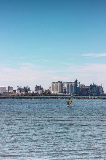 Sea by buildings with person windsurfing in city against sky