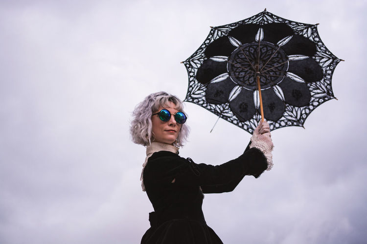 Low angle view of woman holding umbrella against sky