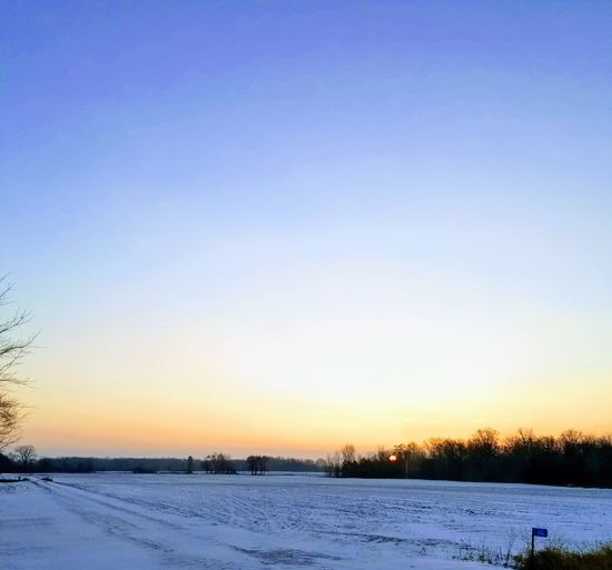 Snow covered field against clear sky during sunset