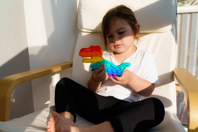 Girl holding toy while sitting on seat at home