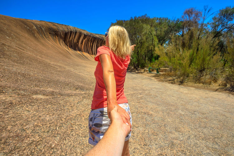 Rear view of women holding hand of man while standing against rock formation 