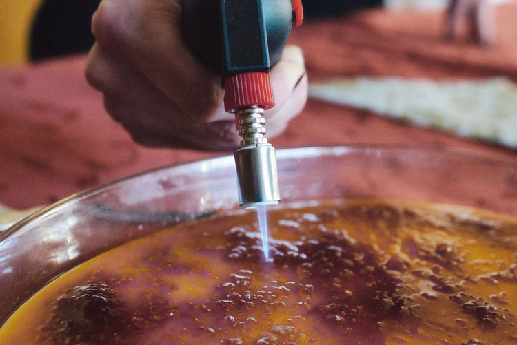 Close-up of hand preparing creme brulee with burner
