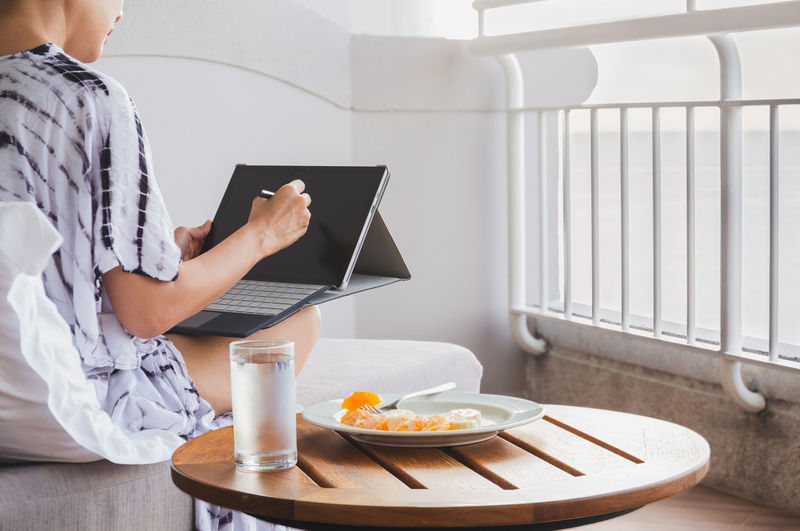 Woman woking on tablet laptop computer with glass of water and fresh fruit on table