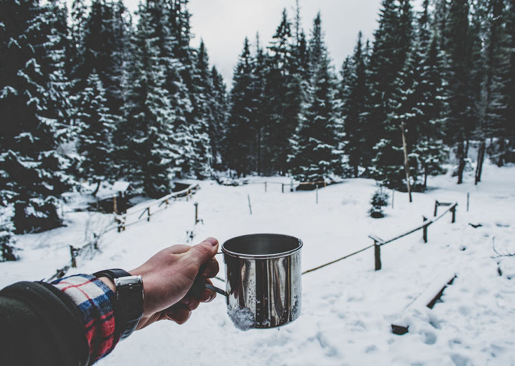 Cropped hand holding mug on snow covered field during winter