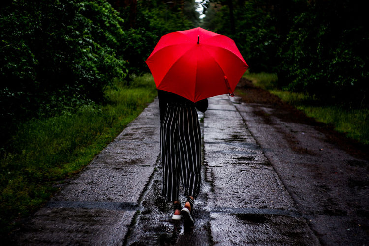 Rear view of woman standing on wet footpath during rainy season
