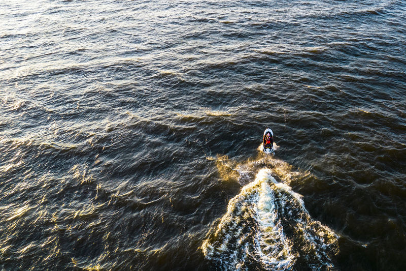Aerial view of man rides on fast water scooter jumping on waves and making golden splashes on sunset