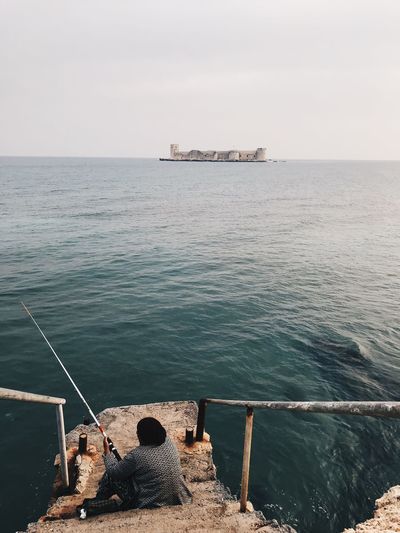 Woman fishing in sea against clear sky