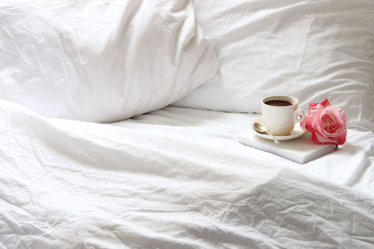 Coffee cup and rose on bed at home