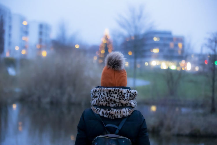 Rear view of woman against illuminated city during winter