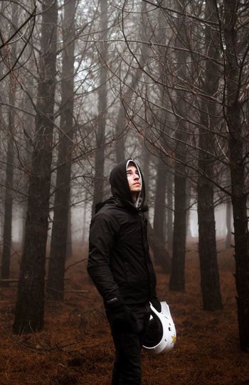 Young man with helmet standing in forest during foggy weather