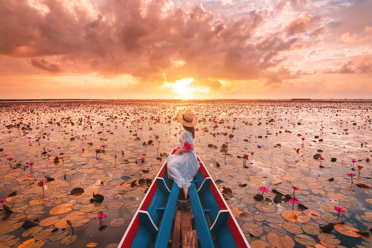 Full length of woman siting on rowboat in lake during sunset