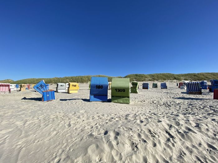 Hooded beach chairs on sand against clear blue sky
