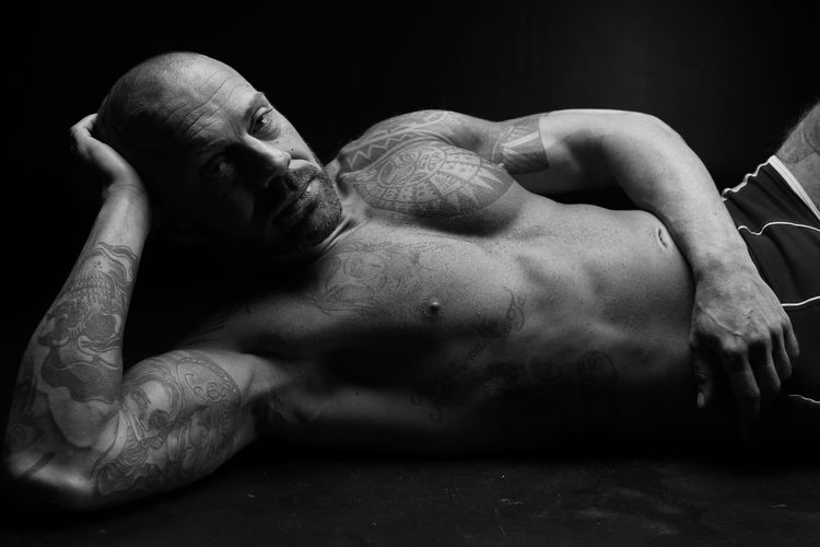 Portrait of shirtless man lying on black background