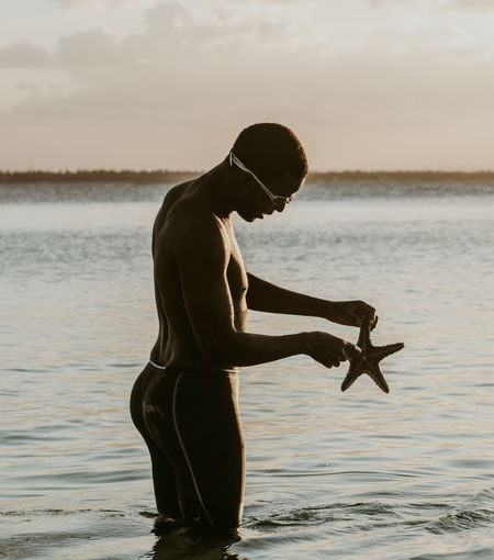 Portrait of a young man holding a starfish in the ocean during sunset
