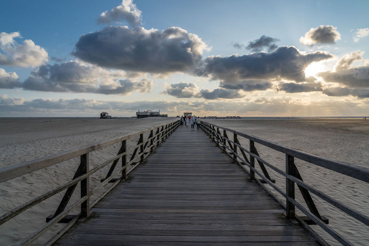 Boardwalk leading towards sea against sky during sunset