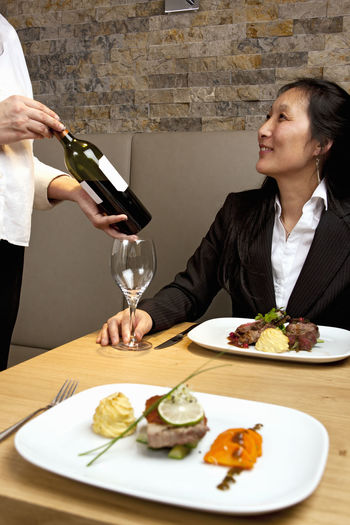 Waiter presenting red wine to business woman at luxury restaurant