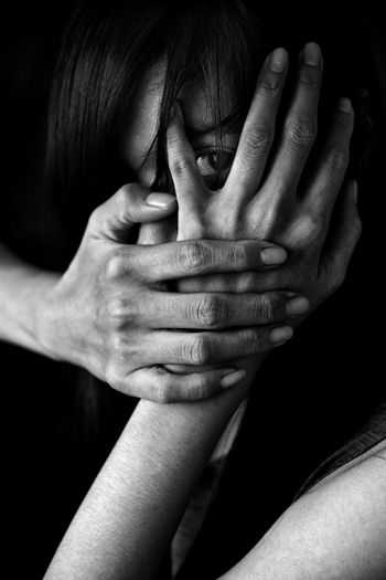 Portrait of woman covering face with hand against black background