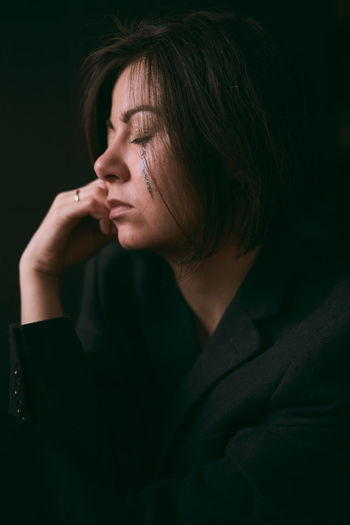 Close-up portrait of young woman looking away over black background