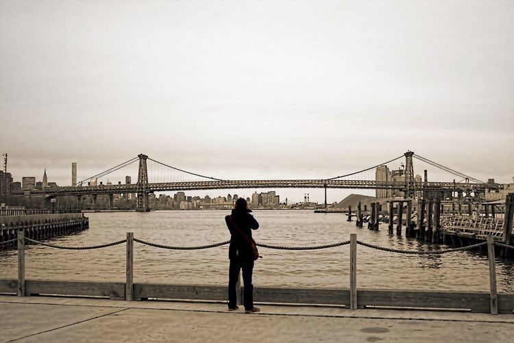 Rear view of man standing in front of williamsburg bridge over east river