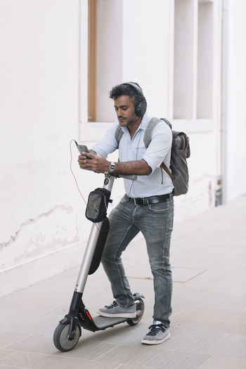 Casual businessman with headphones, smartphone and e-scooter in the city