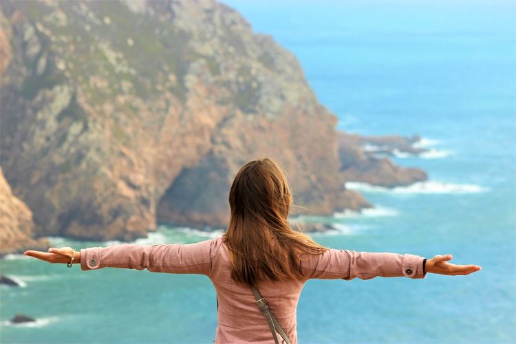 Rear view of woman with arms outstretched standing against sea