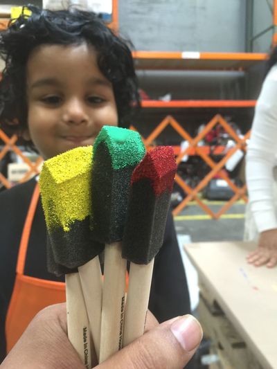 Cropped hand holding paintbrushes against cute boy in background